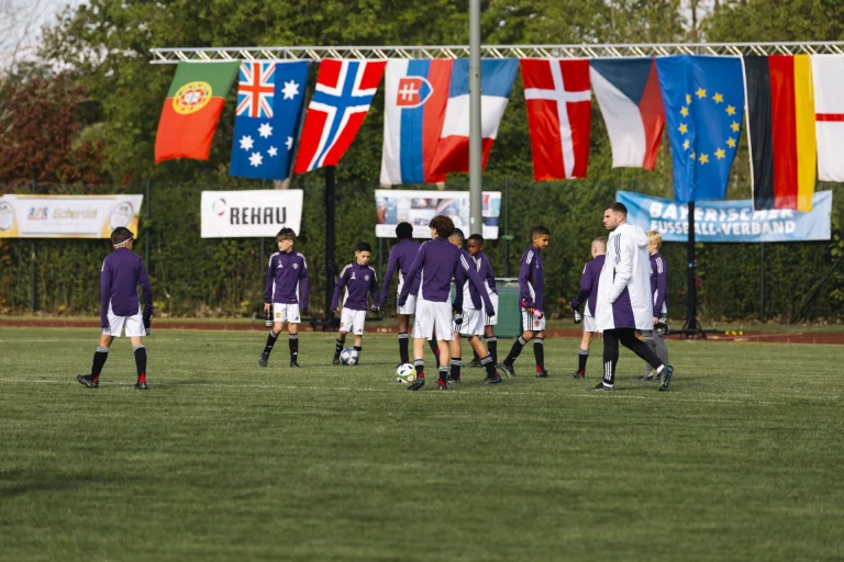 Fußballmannschaft in violetten Trikots beim Aufwärmen vor Länderflaggen auf dem Sportplatz