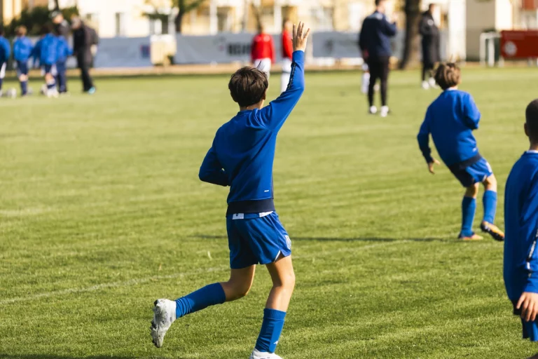 Junge im blauen Trikot läuft mit erhobener Hand über den Fußballplatz