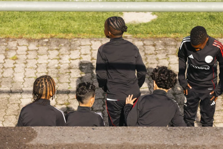 Jugendliche in schwarzen Trainingsanzügen stehen und sitzen auf der Tribüne