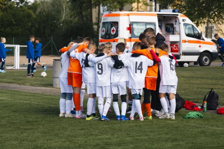 Kindermannschaft im Mannschaftskreis auf dem Spielfeld, im Hintergrund ein Rettungswagen
