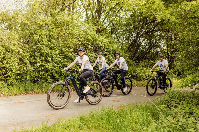 Vier Personen mit Fahrradhelmen fahren hintereinander auf E-Bikes einen Weg entlang