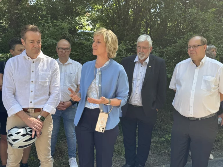Frau im Gespräch mit mehreren Personen am Flüsseradweg, ein Mann hält einen Fahrradhelm