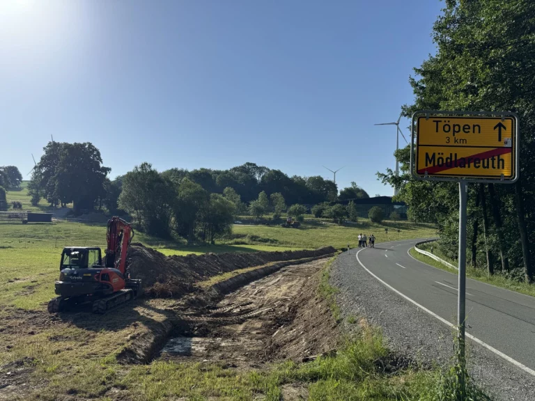 Bagger hebt Graben neben der Kreisstraße aus, Ortsschild Mödlareuth am Fahrbahnrand
