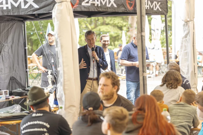 Mann mit Mikrofon spricht zu Sitzenden unter einem Pavillonzelt beim Zeltlager