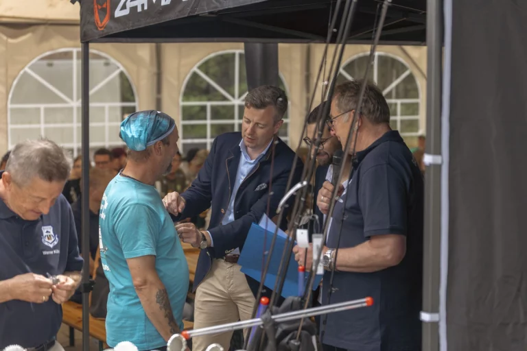 Teilnehmer und Betreuer begutachten Angelausrüstung an einem Stand im Festzelt