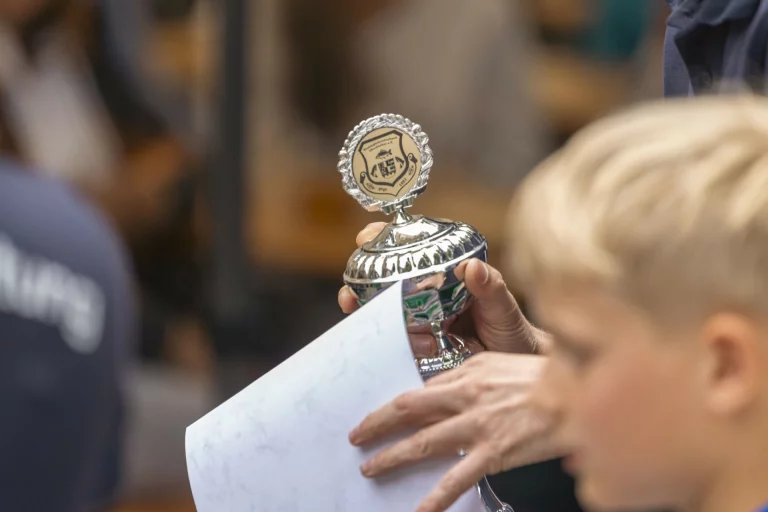 Hand überreicht Jugendlichem einen silbernen Pokal mit Vereinswappen