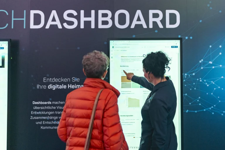 Zwei Frauen betrachten ein digitales Dashboard mit regionalen Daten auf einem Bildschirm