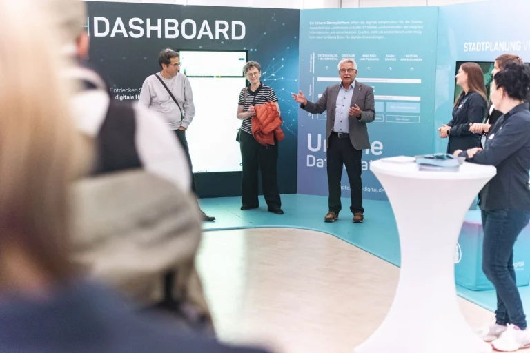 Mann erklärt Dashboard zur Stadtplanung vor Besuchergruppe im InnovationsRAUM