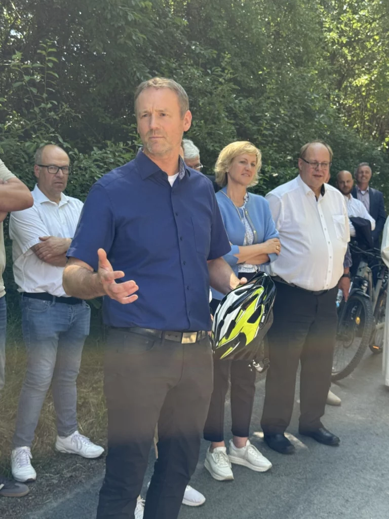 Mann in blauem Hemd spricht bei der Einweihung des Flüsseradwegs, umgeben von Zuhörern