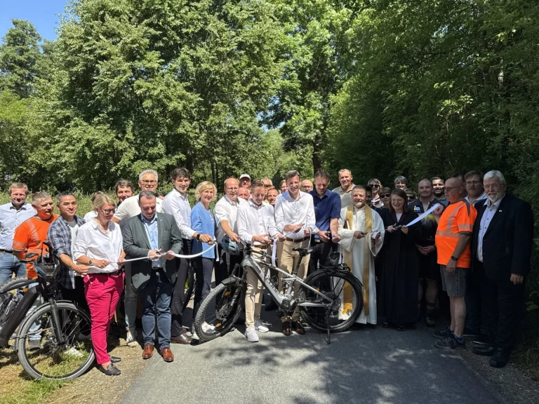 Gruppe von Personen durchschneidet Band an neuem Radweg zwischen Bäumen