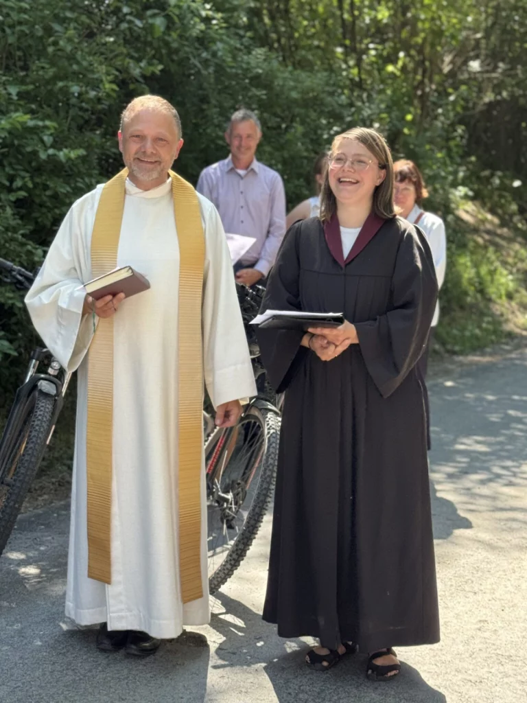 Pfarrerin und Pfarrer mit Fahrrädern stehen lachend auf dem neuen Radwegabschnitt