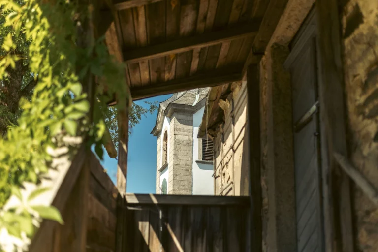 Blick durch einen Torbogen auf einen verschieferten Kirchturm in Hallerstein