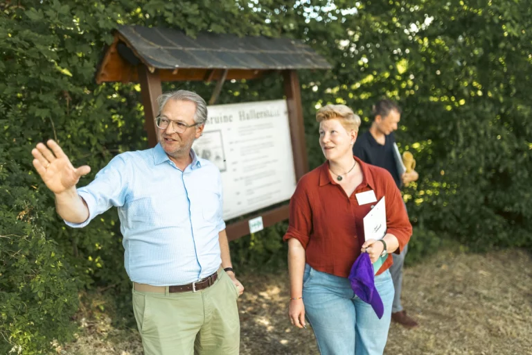 Mann erklärt am Infoschild zur Ruine Hallerwald, Frau und weitere Person hören zu