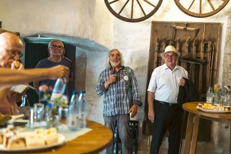 Gruppe von Männern bei einer Zusammenkunft im Innenraum eines historischen Gebäudes mit Getränken und Gebäck