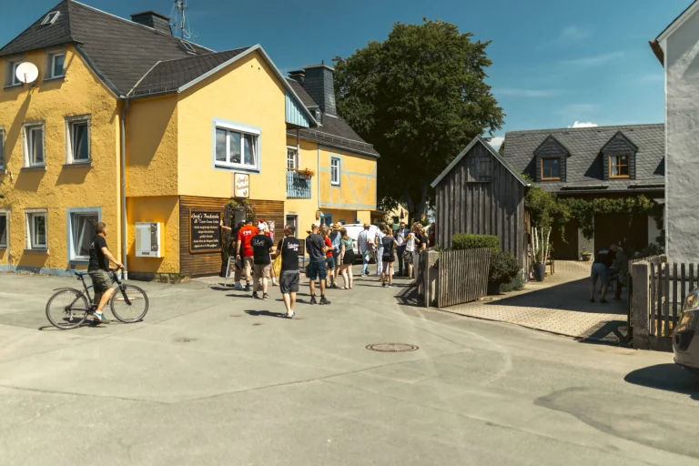 Gruppe von Personen vor gelbem Haus in Hallerstein, im Vordergrund Mann mit Fahrrad