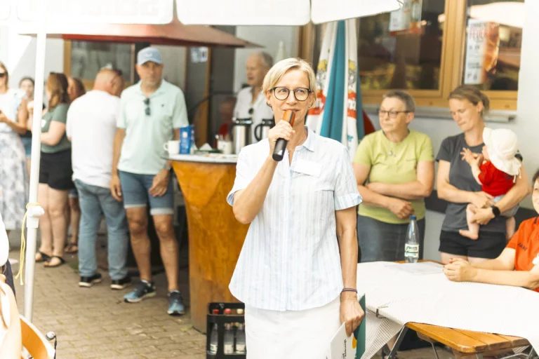 Frau mit Mikrofon spricht zu Gästen bei einer Veranstaltung im Freien