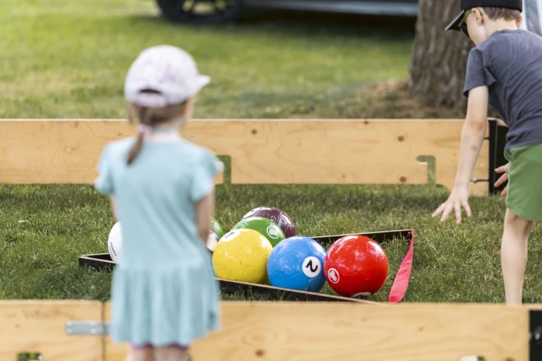 Kinder spielen mit bunten Kugeln an einer Boule-ähnlichen Bahn im Freien