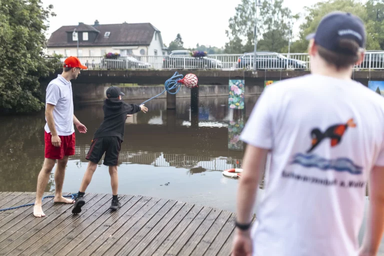 Jugendliche werfen einen Rettungsring an der Selbitz, im Hintergrund eine Brücke