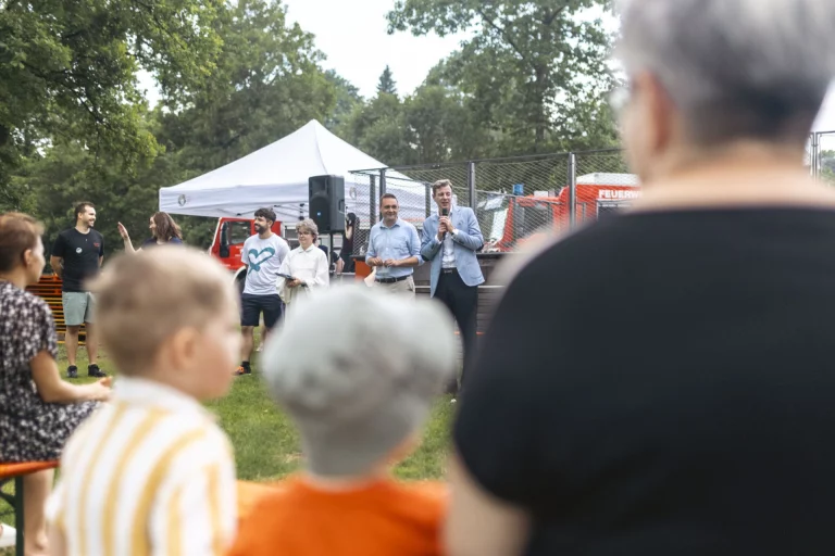 Rednerpult mit Mikrofon vor Festzelt und Feuerwehrfahrzeugen, davor sitzende Kinder und Erwachsene