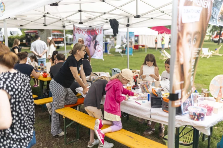 Kinder und Erwachsene an Bastel- und Infoständen unter Pavillons auf einer Wiese
