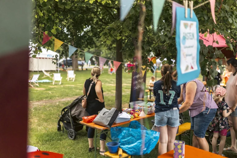 Menschen an Imbissständen mit Wimpelgirlanden unter Bäumen auf einer Wiese