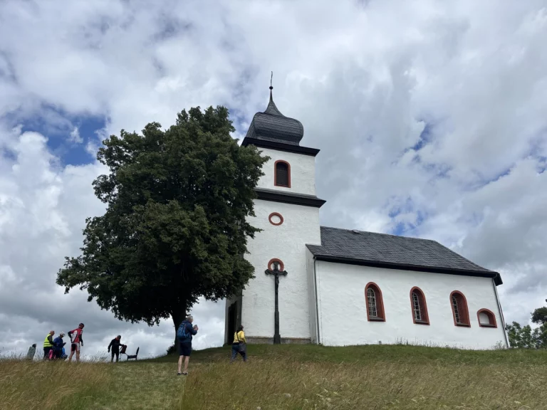Personen vor einer Kirche mit Zwiebelturm auf einer Anhöhe bei Heinersgrün