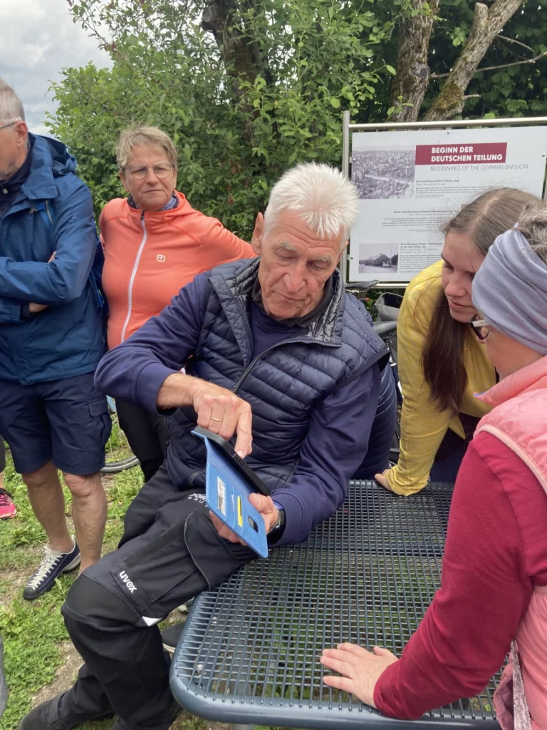 Teilnehmer an einer Informationstafel zur deutschen Teilung, Blick auf ein Tablet mit historischem Foto