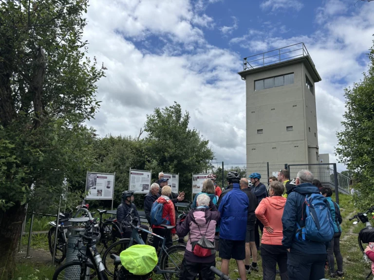 Gruppe mit Fahrrädern vor einem ehemaligen Grenzturm bei einer Infotafel-Führung