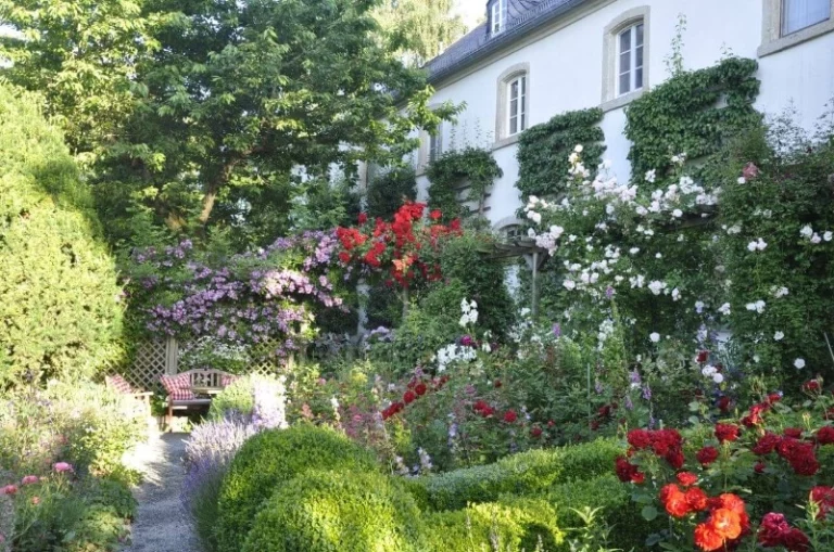 Blühender Schlossgarten mit Rosenbögen, Kletterrosen an Fassade und Staudenbeeten