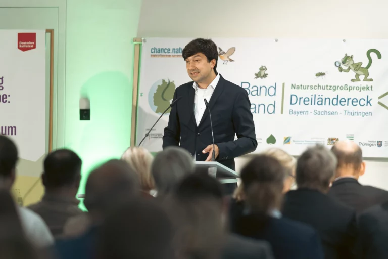 Mann hält Rede am Rednerpult vor Banner „Grünes Band Dreiländereck“, davor sitzendes Publikum