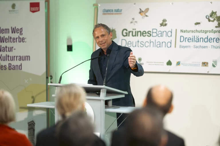 Mann am Rednerpult vor Bannern zu Grünes Band Deutschland, dahinter sitzendes Publikum