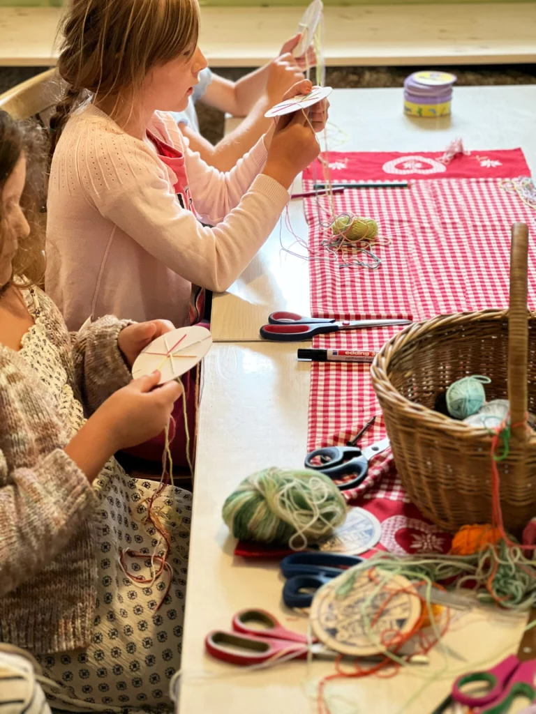 Kinder flechten Wollfäden auf runden Webkarten an einem Tisch mit Schere und Garn