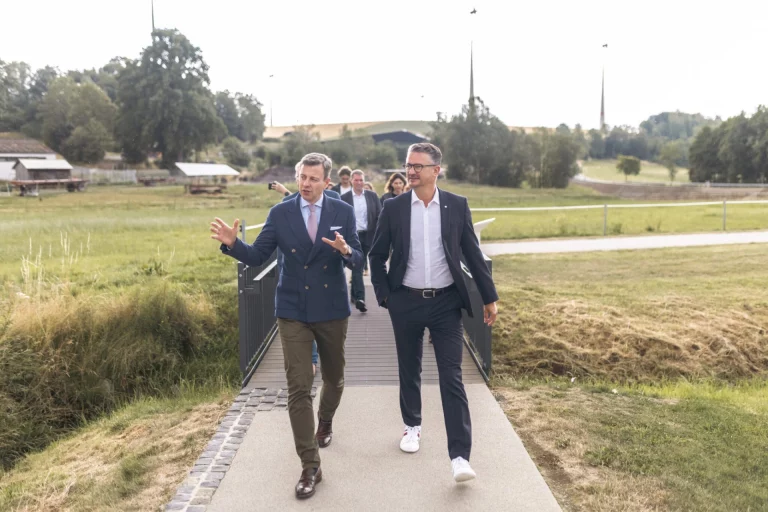 Zwei Männer im Gespräch auf einem Steg über eine Wiese bei Mödlareuth, weitere Personen folgen