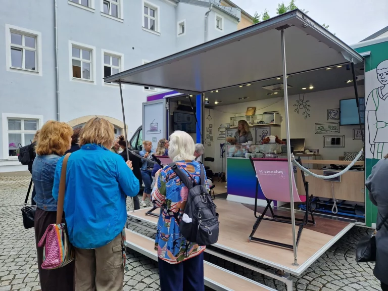 Gruppe von Personen vor einem mobilen Beratungsstand mit Theke und Beraterin
