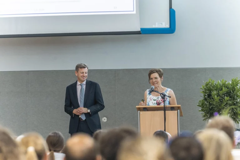Mann und Frau am Rednerpult sprechen vor Publikum im Saal