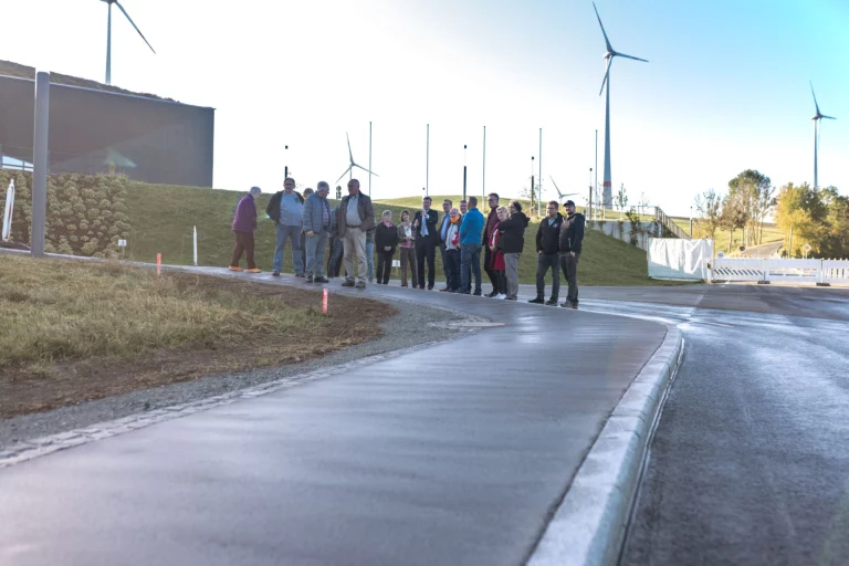 Gruppe von Personen begutachtet neu asphaltierten Gehweg entlang der Straße bei Windrädern