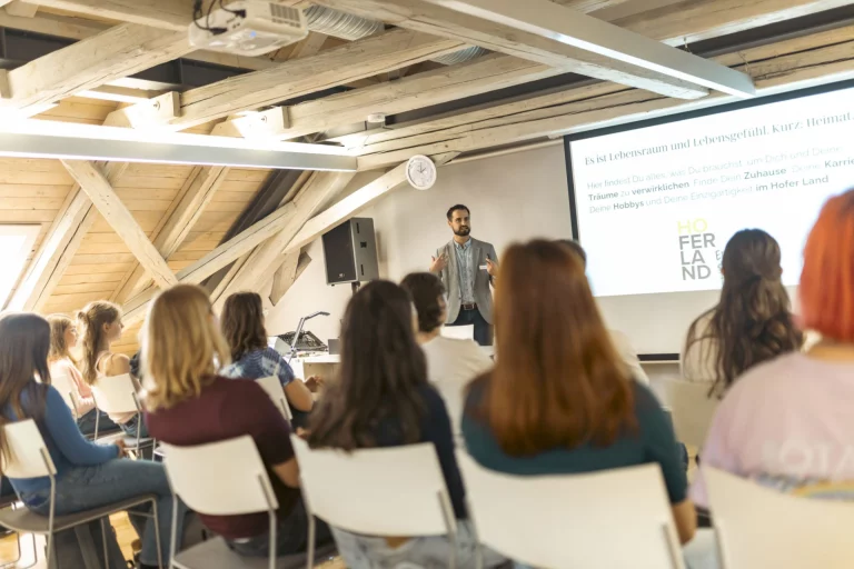 Mann spricht vor sitzenden Teilnehmerinnen in einem Workshop mit Präsentation zum Hofer Land