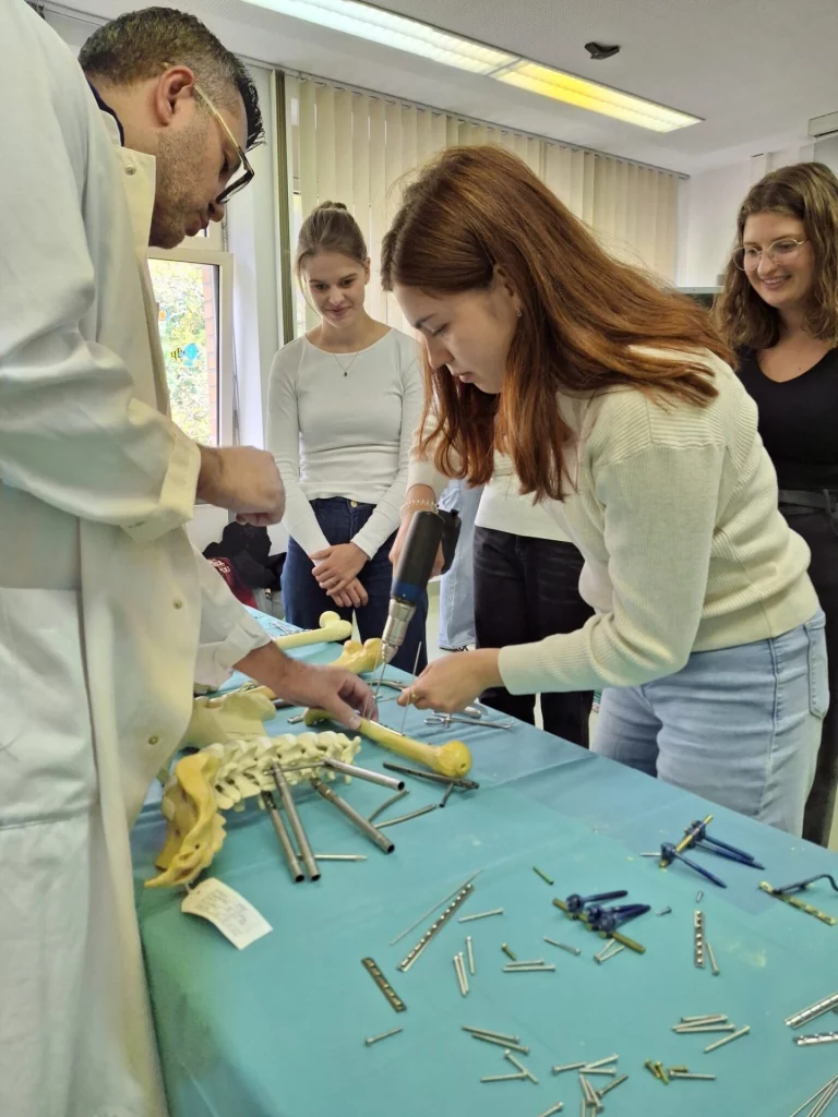 Person demonstriert Osteosynthese-Material an Wirbelsäulenmodell, Studierende schauen zu