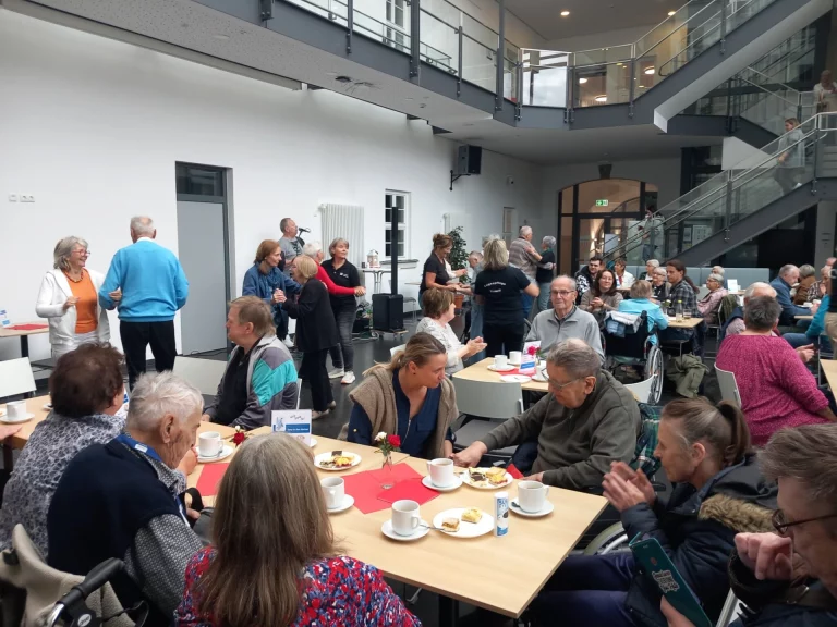 Gruppe von Menschen an gedeckten Tischen im Foyer, im Hintergrund tanzende Paare
