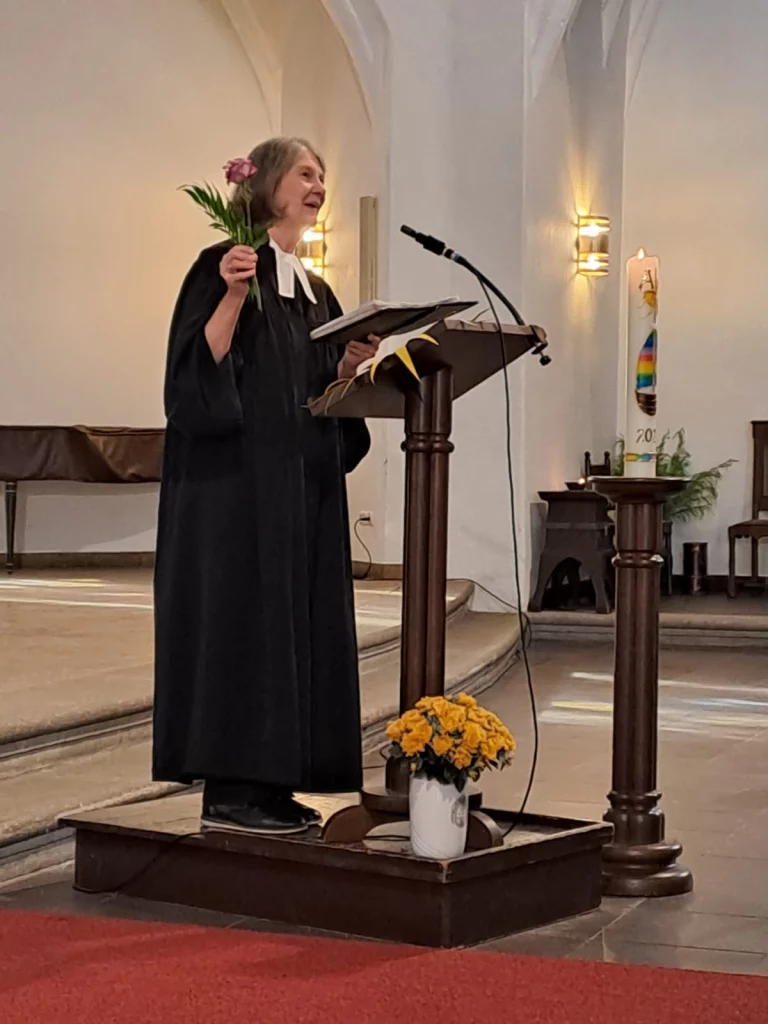Pfarrerin mit Blume in der Hand spricht am Lesepult in der Kirche